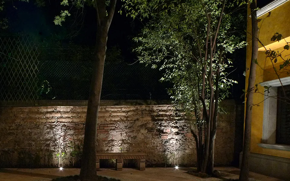 B Residence garden — uplit trees and a grazed brick wall at night