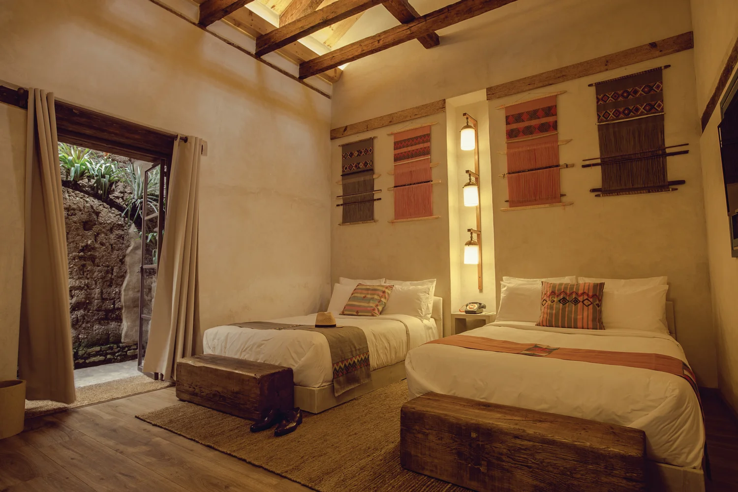 Twin guestroom with skylight beams and woven textile wall hangings