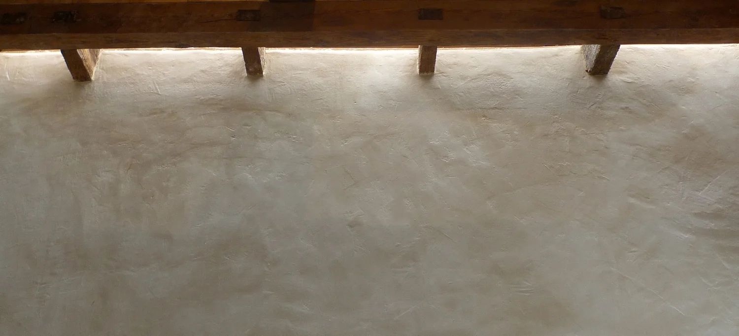 Grazing light washing a hand-finished plaster wall beneath timber beams