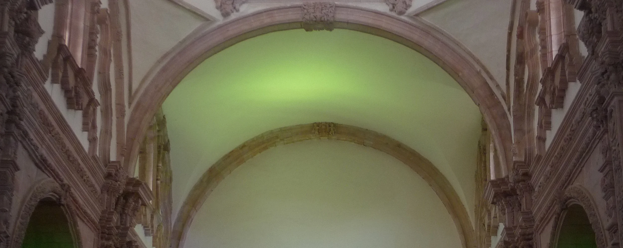 Vaulted ceiling washed in green light between carved arches