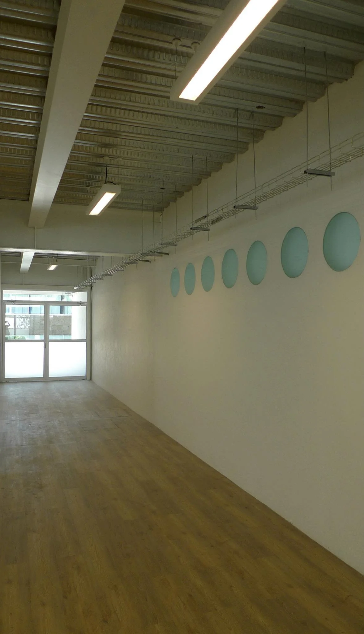 Corridor lined with a wall of translucent discs and suspended linear fixtures
